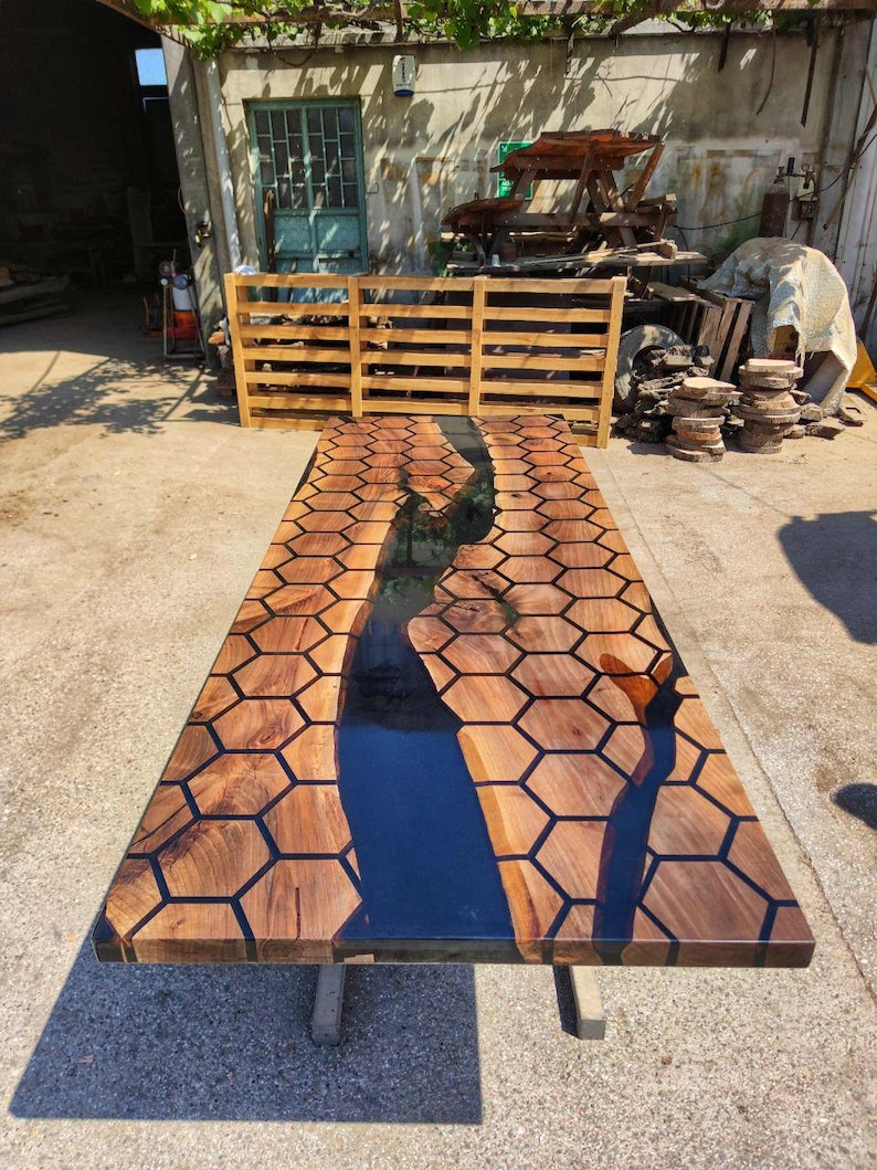 Puede incluir: Una mesa de madera rectangular grande con un dise&ntilde;o &uacute;nico. La superficie presenta un patr&oacute;n de panal con resina oscura que rellena los espacios. Un r&iacute;o de resina azul oscuro recorre el centro. La mesa est&aacute; soportada por patas de metal.