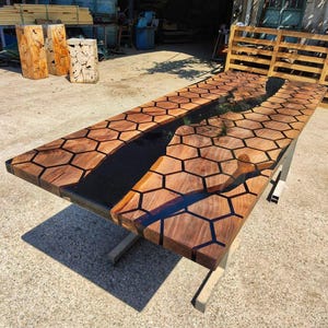 Puede incluir: Una mesa de madera rectangular grande con un dise&ntilde;o &uacute;nico. La tapa de la mesa presenta un patr&oacute;n de panal y una incrustaci&oacute;n de resina epoxi oscura en forma de r&iacute;o. La mesa est&aacute; soportada por una base de metal. La mesa mide unos 244 cm de largo.