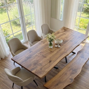 Könnte beinhalten: Ein Esstisch aus Holz mit einem Live-Edge-Design, gepaart mit einer passenden Bank und vier gepolsterten Stühlen. Der Tisch hat eine natürliche Holzmaserung. Eine Vase mit Blumen und eine Schale stehen auf dem Tisch.