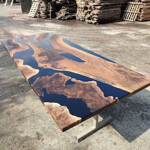 May include: A large wooden table top with black epoxy resin filling in the natural wood grain. The table top is supported by a single metal leg.