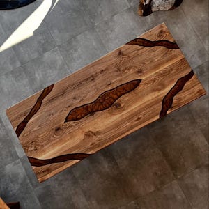 May include: A rectangular wooden coffee table with a natural wood grain finish. The table features dark brown epoxy resin river-like accents. The table is approximately 60 inches long and 30 inches wide.