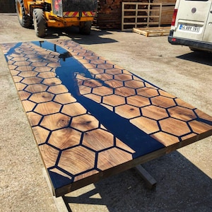 Puede incluir: Una mesa de madera rectangular grande con un dise&ntilde;o &uacute;nico. La superficie de la mesa presenta un patr&oacute;n de panal con resina oscura que rellena los huecos. Un r&iacute;o de resina oscura fluye por el centro. La mesa est&aacute; sostenida por una base met&aacute;lica simple.