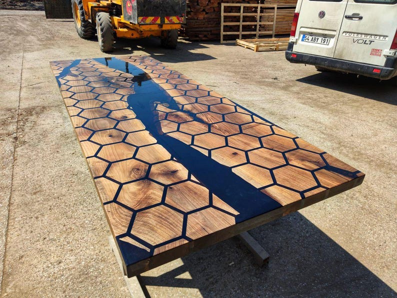 Puede incluir: Una mesa de madera rectangular grande con un dise&ntilde;o &uacute;nico. La superficie de la mesa presenta un patr&oacute;n de panal con resina oscura que rellena los huecos. Un r&iacute;o de resina oscura fluye por el centro. La mesa est&aacute; sostenida por una base met&aacute;lica simple.