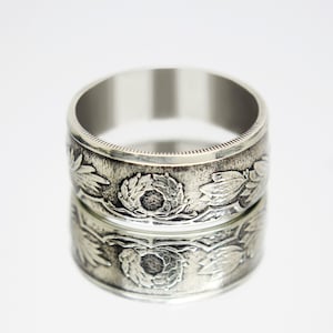 Peut inclure: Une bague en argent fabriquée à partir d'une pièce de monnaie avec un motif floral. La bague est large et a une finition lisse et polie.