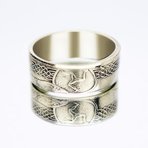 Peut inclure: Bague argentée avec un design détaillé. La bague présente un emblème central d'une figure en course dans un cadre circulaire, complété par des motifs de nœuds celtiques complexes. La surface de la bague reflète le motif, créant un effet miroir.