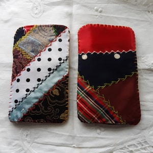 May include: Two rectangular patchwork fabric cases. One features a mix of patterned fabrics, including polka dots, paisley, and floral designs, stitched together with red and black thread. The other case has a red top, navy blue center, and plaid and burgundy bottom.