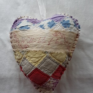 May include: A heart-shaped quilted ornament with a patchwork design in various colors, including purple, blue, yellow, and red. The ornament has a white ribbon for hanging and a fabric strip with the text "With Lots of Love".
