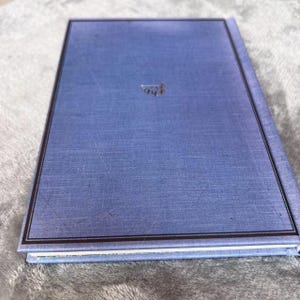 Puede incluir: Un diario de tapa dura azul con un borde negro y un dise&ntilde;o en relieve plateado en la portada.