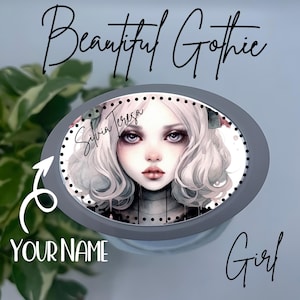 May include: A gray oval phone grip with a white background featuring a black and white illustration of a girl with long white hair and a black dress. The text "Silvia Teresa" is written in black cursive on the image. The text "Beautiful Gothic Girl" is written in black cursive above the phone grip. The text "YOUR NAME" is written in black cursive below the phone grip.