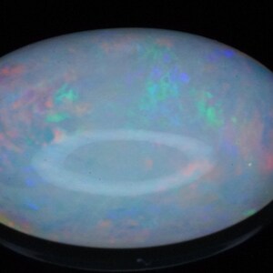 May include: An oval-shaped cabochon opal gemstone featuring a translucent white base with a vibrant play-of-color, displaying flashes of red, green, and blue light throughout the surface against a dark background.