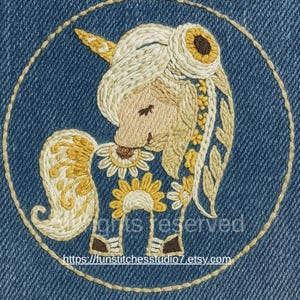 Puede incluir: Parche bordado con un unicornio caprichoso con cuerno dorado, melena y detalles de girasoles. El diseño está sobre un fondo de mezclilla azul y enmarcado por un círculo cosido. El texto "rights reserved" y una dirección web son visibles.