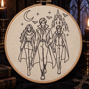 Puede incluir: Un bastidor de bordado circular de madera que contiene un panel de tela color crema con arte lineal en hilo negro. El diseño muestra tres figuras estilo anime con abrigos largos, una luna creciente, estrellas, murciélagos y un castillo.