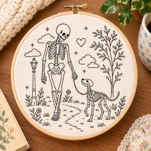 May include: A circular wooden embroidery hoop containing a white fabric panel with black line art. The design features a skeleton walking a skeletal dog on a leash in a park setting with a lamp post, a tree, clouds, flowers, and a heart.