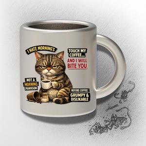 Puede incluir: Una taza de café de cerámica plateada con un gato de dibujos animados gruñón sosteniendo una taza de café. La taza tiene texto que dice "I hate mornings", "Touch my coffee... and I will bite you" y "Before coffee: grumpy & dislikable".
