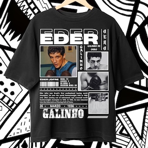 May include: A black short-sleeve t-shirt featuring a graphic print of boxer Eder Jofre. The design includes multiple black and white photographs of the athlete, the text EDER GALINHO DE OURO, career statistics, and a biographical paragraph about his boxing history.