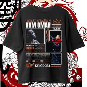 Puede incluir: Camiseta negra con un diseño gráfico que presenta un retrato del músico Dom Omar, el texto "Dom Omar", "El Rey", "Kingdom" y "New EP". El gráfico también incluye una corona y el texto "Dile", "My Space", "Hooka", "Ojos Chiquitos" y "Quaya Quaya".