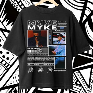 Puede incluir: Camiseta negra con un diseño gráfico que incluye el texto "MYKE MYKE" y una foto de un hombre con una camisa a rayas azul y blanca. El texto "YOUNG KINOZ 2024" y "Myke Towers" también están incluidos en el diseño. El texto "NEW EP" y una lista de títulos de canciones también están incluidos en el diseño.