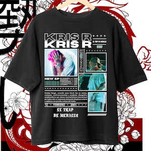 以下が含まれることがあります： ピンクの髪の男性の肖像画と「Kris R」と「El Trap de Medallo」のテキストが描かれた白いグラフィックデザインが施された黒いTシャツ。