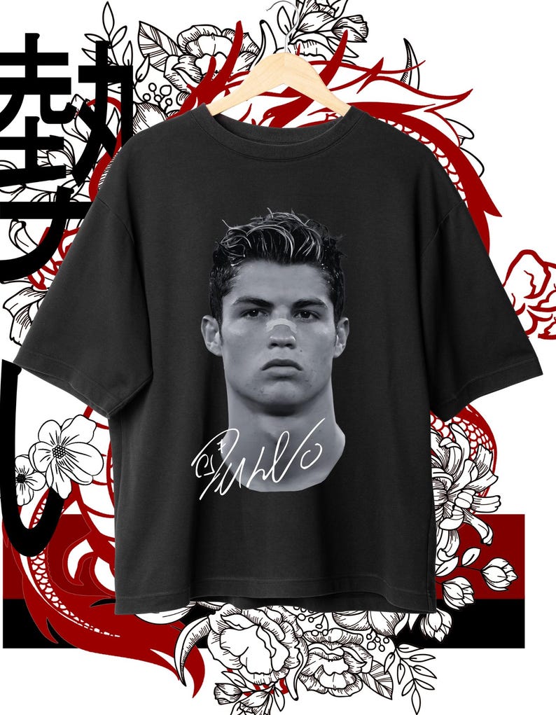 May include: Black t-shirt with a black and white image of a soccer player's face and signature. The signature reads "CR7". The t-shirt is on a hanger against a red and white floral background.