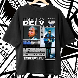 以下が含まれることがあります： 白のグラフィックデザインが施された黒いTシャツ。デザインには、男性の肖像画と、「BEI V」と「DEIV」の文字が太字の白で書かれている。デザインには、「David Geraldo」、「Quien es Dei V?」、「New EP」の文字も含まれている。「26 Diciembre + 1995 + Underwater」の文字はデザインの下部に書かれている。