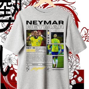 Op de afbeelding: Een grijs T-shirt met een grafisch ontwerp met een foto van voetballer Neymar Jr. Het ontwerp bevat de tekst "Neymar Neymar" in zwart en wit, en "Ney 10" in zwart. De tekst "5 Febrero 1992" is ook in het ontwerp opgenomen.