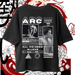 May include: Black t-shirt with a white graphic design featuring the text "ARC" and "ALL WE NEED IS LOVE". The graphic also includes a barcode, a triangle with the text "An SER BERD", and a circle. The text "CAISEREBRO TIRONE 2015" is also included in the graphic.