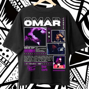 Puede incluir: Camiseta negra con un diseño que presenta el nombre "OMAR" en blanco. La camiseta incluye imágenes y texto sobre Omar Courtz, un cantante y compositor puertorriqueño. El diseño incorpora acentos morados y blancos.