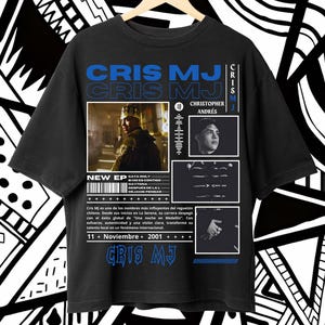 May include: Black t-shirt featuring the text "CRIS MJ" in blue, with additional text and images. The shirt includes a photo of a person wearing a crown and other graphics. The shirt also has the text "NEW EP".