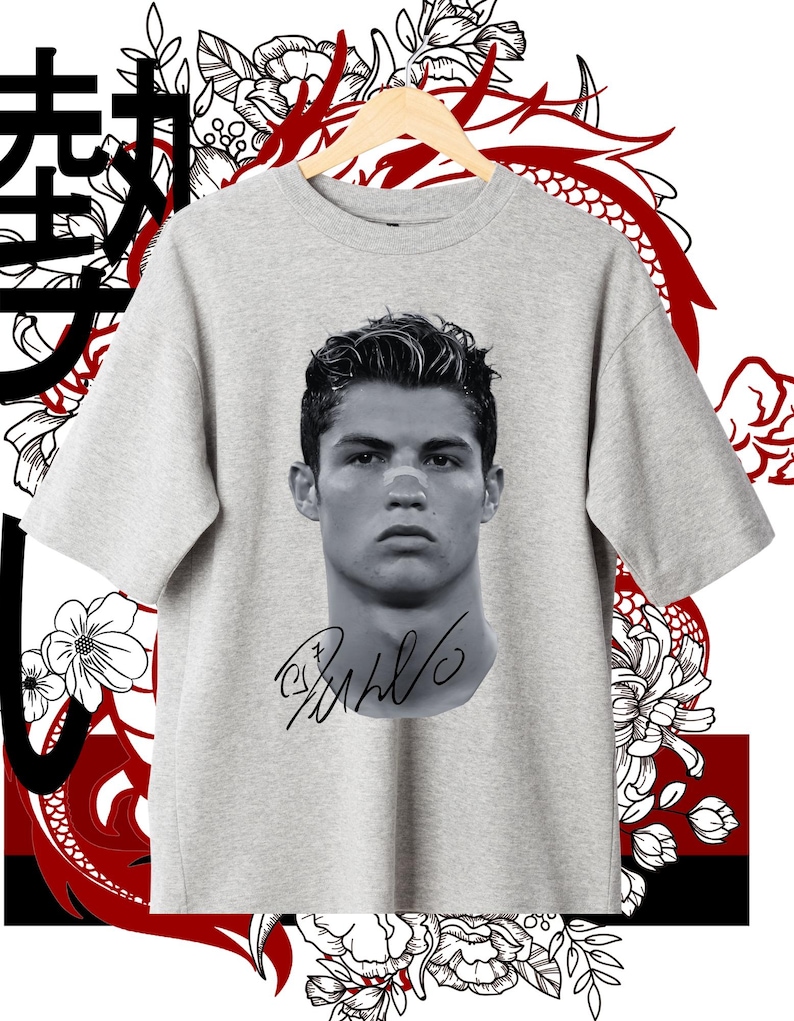 May include: A gray t-shirt with a black and white image of a soccer player's face and signature. The player's name is Cristiano Ronaldo. The t-shirt has a Japanese character on the left side of the image.