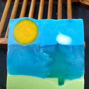 May include: A blue and green soap bar with a yellow sun, a white cloud, and a green tree design.