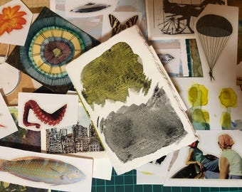 May include: A collection of various art prints and stickers. The image features a watercolor painting with green and gray tones, along with stickers of a flower, a fish, an octopus tentacle, and other illustrations. The overall theme is artistic and creative.