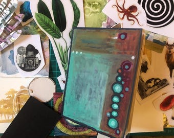 May include: An abstract art journal with a teal and brown painted design, surrounded by various paper ephemera, including botanical illustrations, a deer, and a vintage photograph.