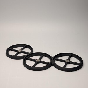 May include: Three black, circular objects with a wheel-like design. Each has a central hub and spokes radiating outwards. Small, silver-colored magnets are visible at the center of each circle. The objects are made of a matte material.