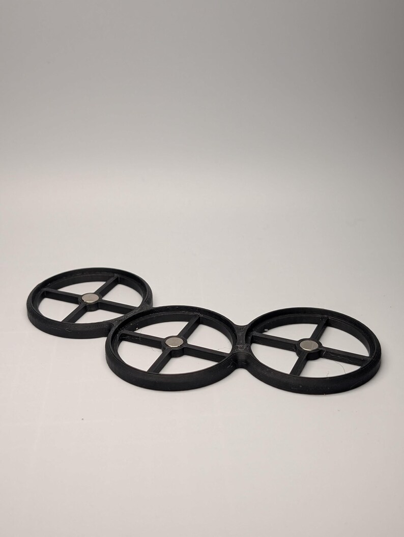 May include: Three black, circular objects with a wheel-like design. Each has a central hub and spokes radiating outwards. Small, silver-colored magnets are visible at the center of each circle. The objects are made of a matte material.