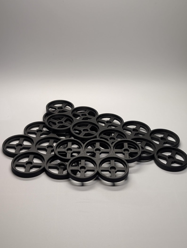 May include: A collection of black, circular objects with a cross-shaped design in the center. The objects are arranged in a pile against a white background. The objects appear to be made of plastic.