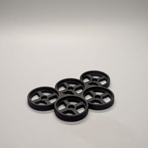 May include: A cluster of six black, circular objects with a wheel-like design. Each object has a central hole and four spokes. The objects are arranged in a slightly overlapping pattern against a white background.