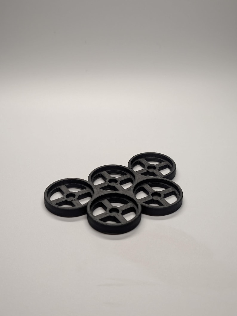May include: A cluster of six black, circular objects with a wheel-like design. Each object has a central hole and four spokes. The objects are arranged in a slightly overlapping pattern against a white background.