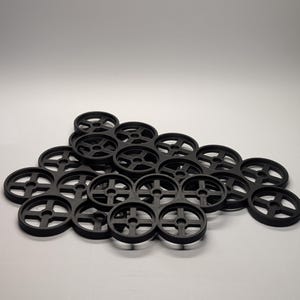 May include: A collection of black, circular objects with a cross-shaped design in the center. The objects are arranged in a cluster, with some overlapping. The items appear to be made of a solid material.