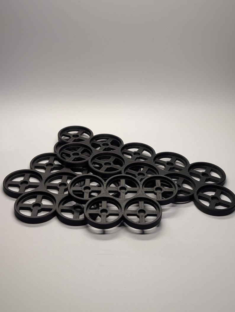 May include: A collection of black, circular objects with a cross-shaped design in the center. The objects are arranged in a cluster, with some overlapping. The items appear to be made of a solid material.