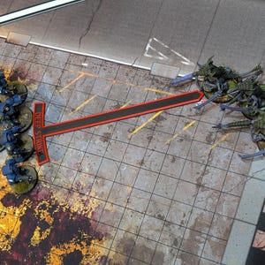 May include: A tabletop game scene featuring miniature figures and a game board. Blue and green figures face each other across a red and black line marked "DEEP STRIKE". The board has a grid pattern and a street-like design.