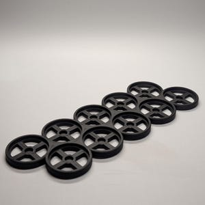 May include: Black plastic drink carrier designed to hold multiple cans or bottles. The carrier has a circular design with a cross-shaped center, and is arranged in a hexagonal pattern. The product is made of a durable material and is suitable for beverages.