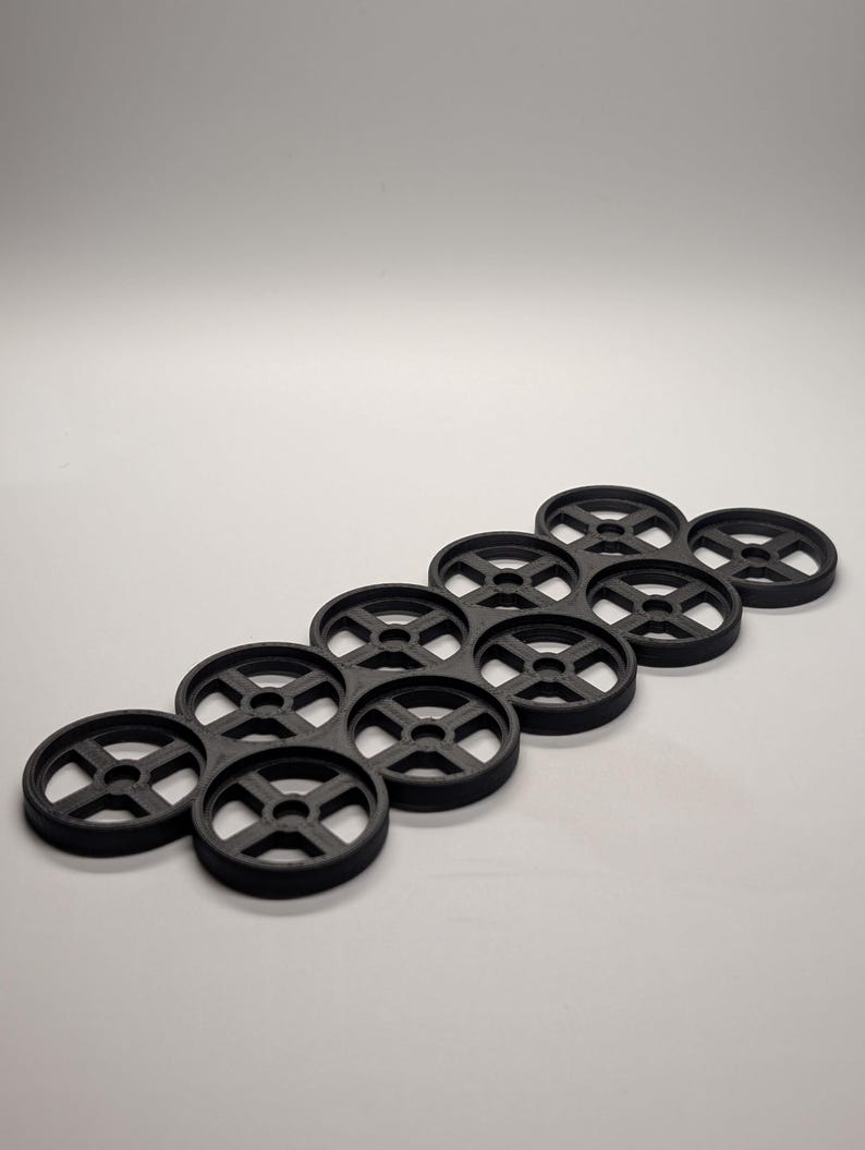 May include: Black plastic drink carrier designed to hold multiple cans or bottles. The carrier has a circular design with a cross-shaped center, and is arranged in a hexagonal pattern. The product is made of a durable material and is suitable for beverages.