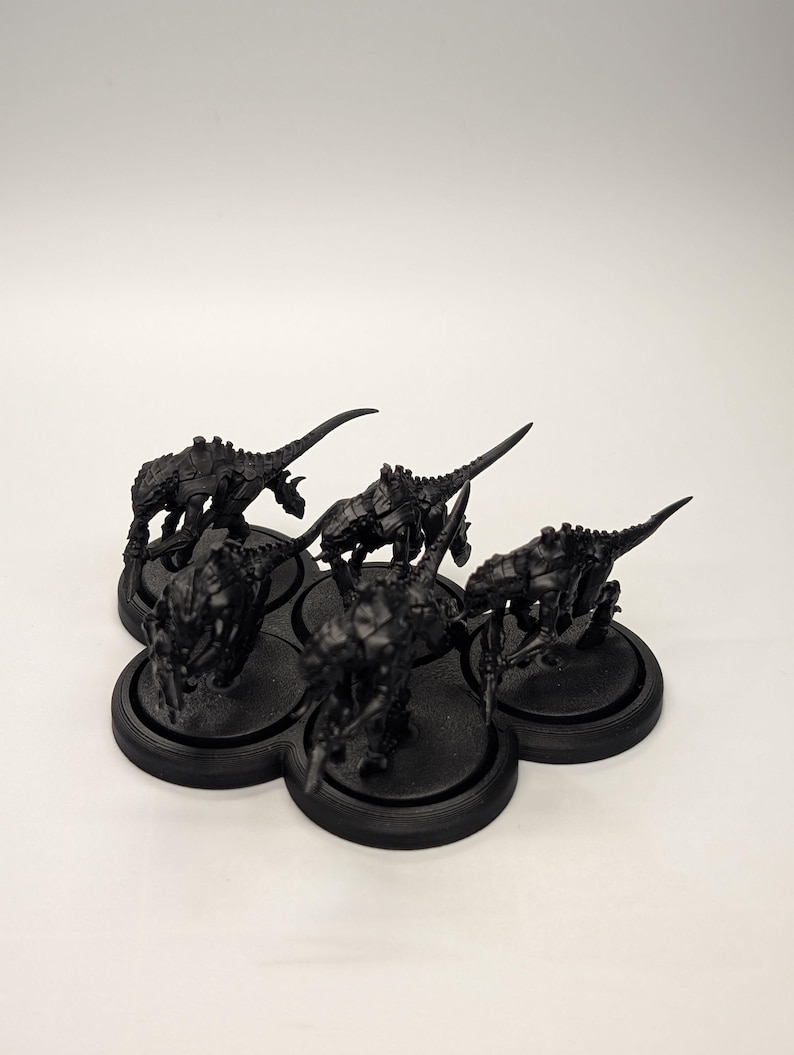 May include: A cluster of six black miniature figurines, each depicting a creature with a spiky, armored body and a long, pointed tail. The figurines are arranged on a black, multi-holed base, set against a white background.