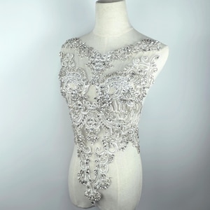 May include: A white mesh fabric applique with a floral design embellished with clear rhinestones. The applique is perfect for adding a touch of sparkle to clothing, bags, or home decor.