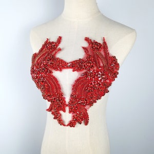 May include: Red beaded applique with a heart-shaped design. The applique is made of red beads and sequins and has a delicate, intricate design.