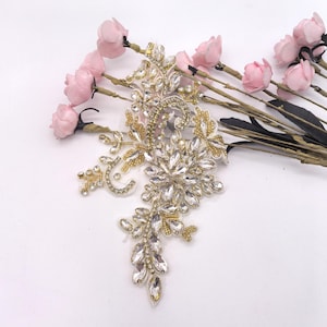 Peut inclure: Une grande applique ornée avec un motif floral en strass dorés et transparents. L'applique est faite d'un tissu transparent et est parfaite pour ajouter une touche d'éclat à n'importe quel vêtement.