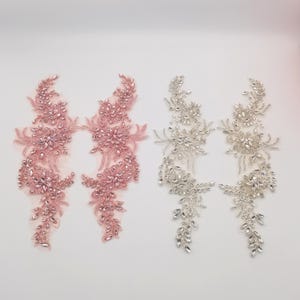 K&ouml;nnte beinhalten: Zwei Paare von Perlen-Applikationen, eine in Rosa und eine in Silber. Jede Applikation zeigt ein florales Design mit kristallartigen Perlen.