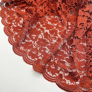 Puede incluir: Primer plano de una tela de encaje de color óxido con un patrón floral. El encaje tiene un borde festoneado.