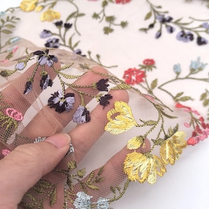 Op de afbeelding: Beige doorschijnend stof met geborduurde bloemenmotieven in tinten roze, geel, blauw en groen.