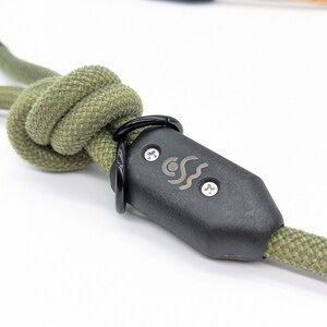 May include: Close-up of a green rope dog leash with a black plastic clasp. The clasp has a silver logo with a wave design and the text "CCS".